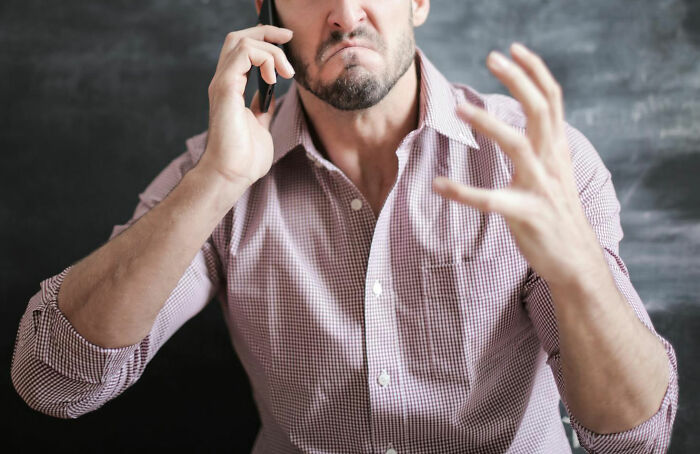 Frustrated man on phone, illustrating revenge on someone in power, wearing checked shirt and gesturing with hand.