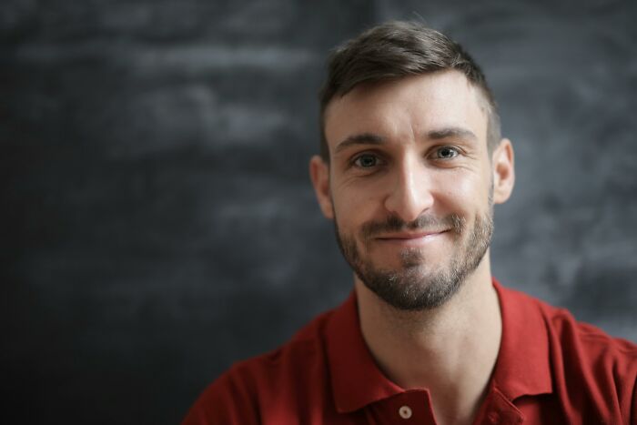Smiling man in a red shirt against a dark background, representing rare cosmetic procedure concepts.
