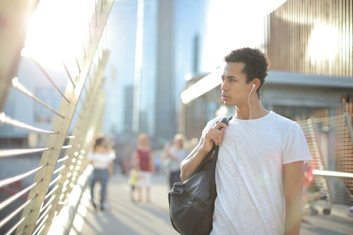 Person in a white shirt and earphones, carrying a backpack, walking in a cityscape under bright sunlight. 2025-Trends.