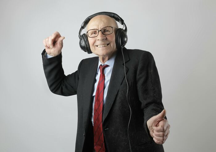 Elderly man in a suit enjoying music with headphones, illustrating a lighthearted moment amid work-struggles.