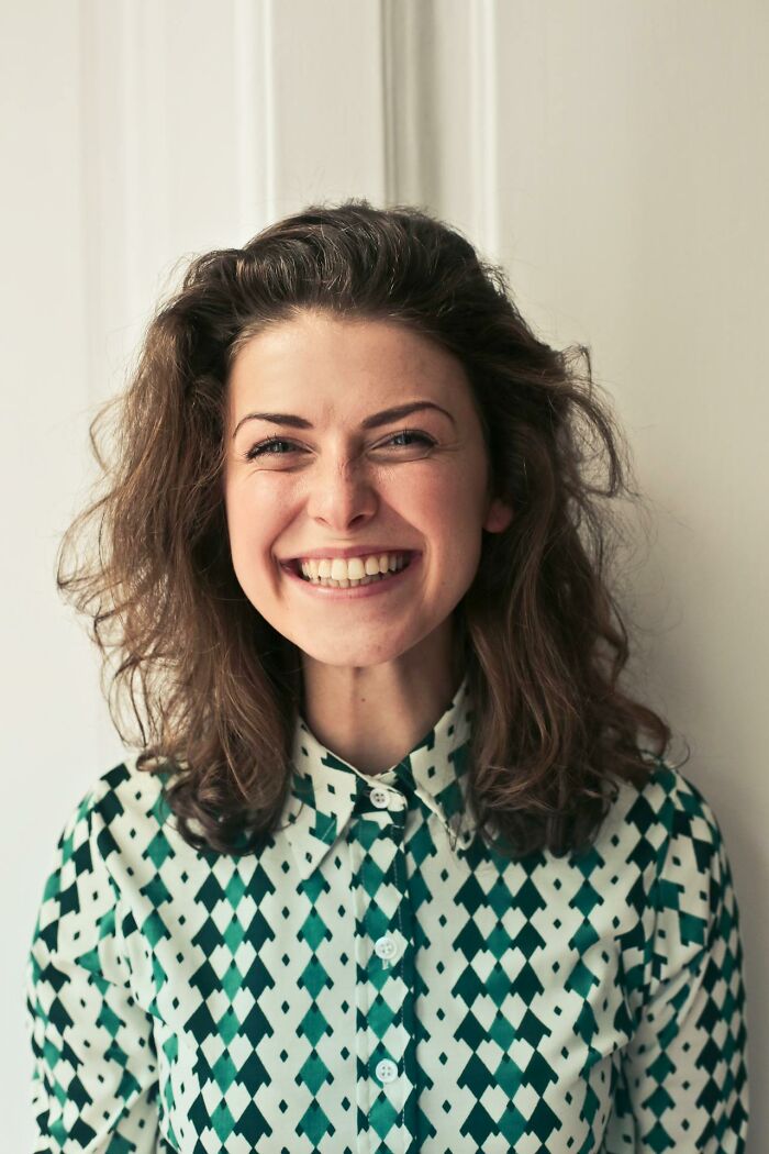 Smiling woman in patterned shirt, showcasing a prominent nose, expressing beauty in unconventional features.