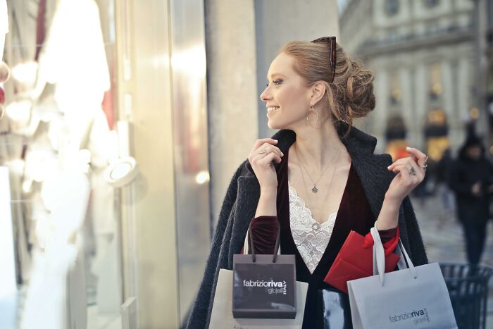 Woman dressed stylishly holding shopping bags, representing things associated with rich people and luxury purchases.