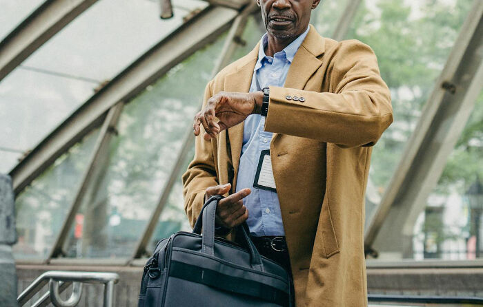 A man in a city setting checks his watch, holding a briefcase, reflecting on the difference between cheap and frugal behavior.