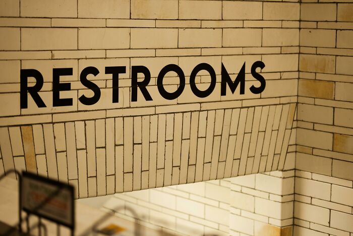 Restroom sign on tiled wall, reminiscent of hilarious overheard conversations in casual settings.