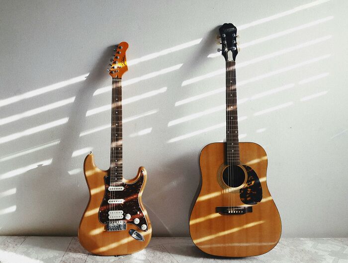 Two guitars, electric and acoustic, rest against a wall, casting striped shadows, illustrating general music knowledge.
