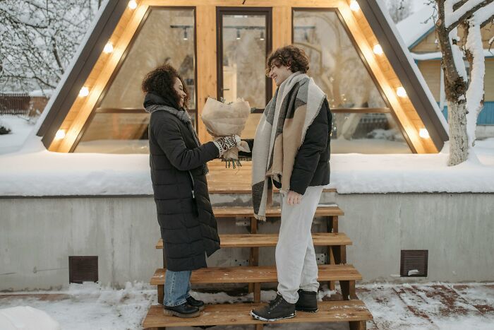 Two people exchanging groceries on snowy steps of a modern house, showcasing winter lifestyle of 2025-Trends.