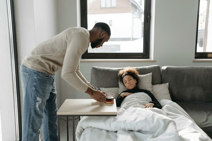 Man serving tea to a woman resting on a couch, capturing an eye-opening moment.