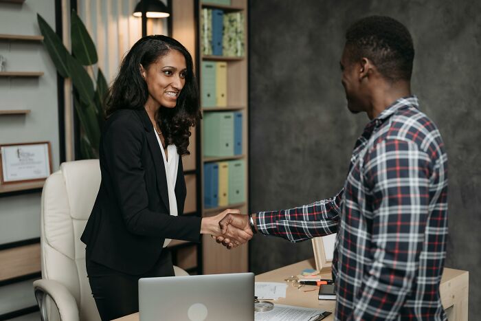 Two professionals shaking hands in an office, highlighting work skills people lack in collaboration and networking.