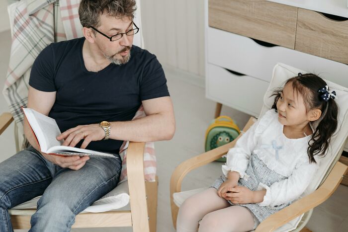 Man reading to a girl, both seated, engaging in a lighthearted moment.