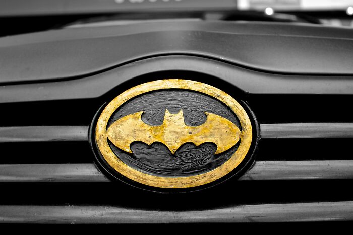 Black and gold Batman emblem on a car grille, humorously symbolizing overheard conversations about superheroes.