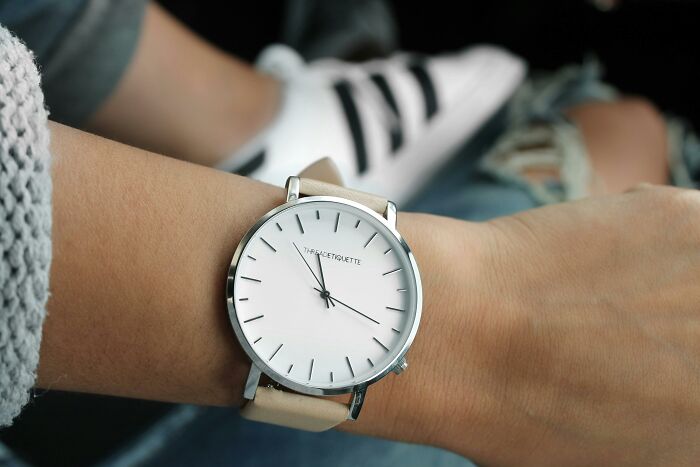 Close-up of a minimalist watch on a person's wrist, with casual sneakers in the background.