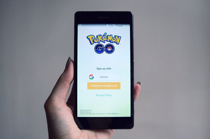 A hand holding a smartphone displaying the Pokémon GO login screen, emphasizing the use of songs as ringtones.