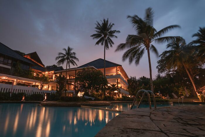 Luxurious estate with illuminated pool and palm trees at dusk, showcasing lifestyle associated with rich people.