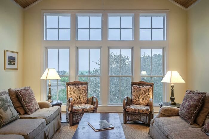 Cozy living room with large windows, two sofas, and two wicker chairs, featuring serene decor.