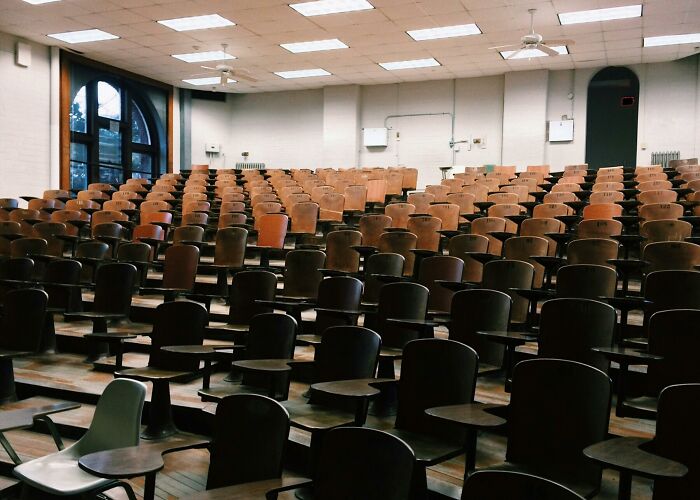 Empty lecture hall with wooden chairs, setting for hilarious overheard conversations.