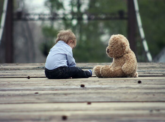 Baby sitting on a wooden deck with a teddy bear, relating to superstitions about growth.