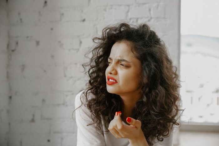 Woman with curly hair and red lipstick, looking puzzled, indoors, discussing creepy family stories.