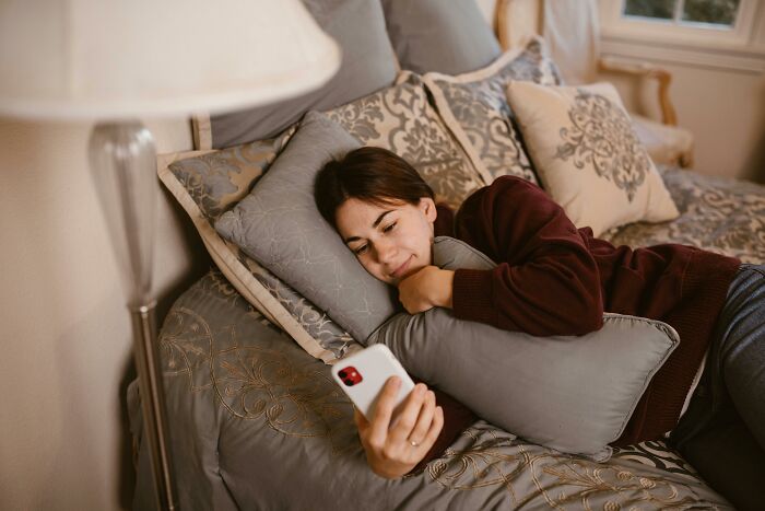 Woman experiencing eye-opening moments while looking at her phone on a cozy bed.