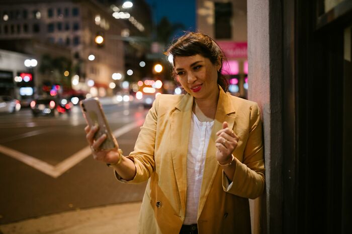 Person taking a selfie on a city street at night, ignoring social rules, wearing a beige blazer.
