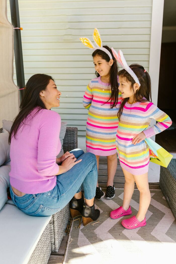 Family moment with a woman and two children in striped dresses wearing bunny ears, enjoying time together on a patio.
