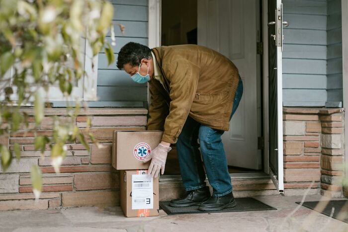 Delivery worker wearing a mask and gloves placing packages outside a home, showcasing perks of not going to the office.