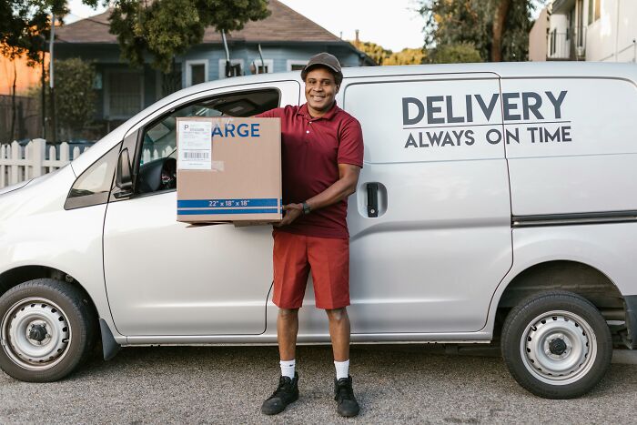 Delivery worker standing by van, holding a package, emphasizing professions people need.