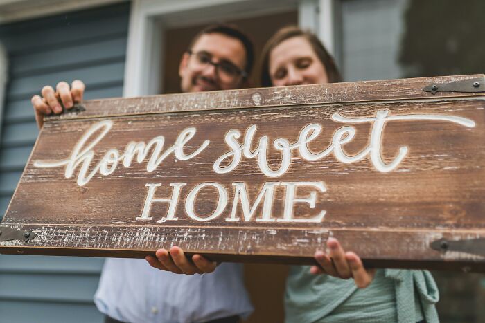 A couple holding a wooden home sweet home sign, representing things associated only with rich people.
