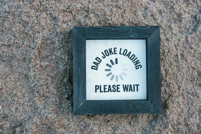 Sign on rock reads "Dad joke loading, please wait," related to hilarious overheard conversations.