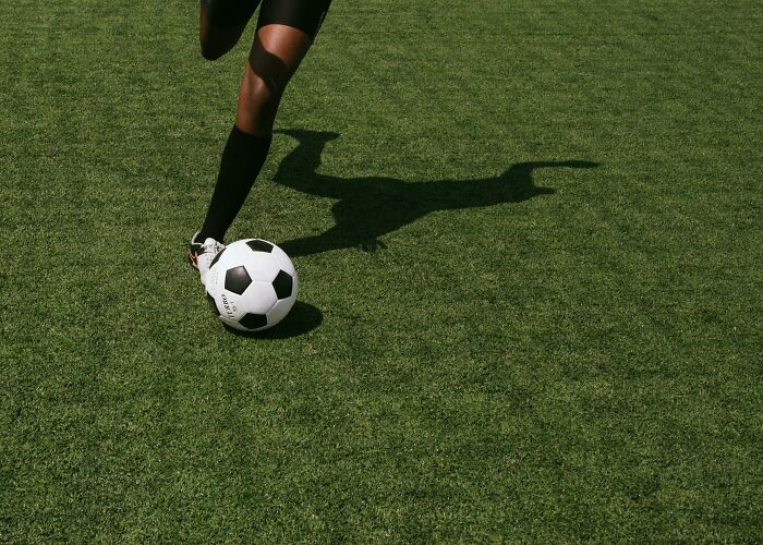 A soccer player in mid-action on a green field, soccer ball in motion, reflecting a shadow.