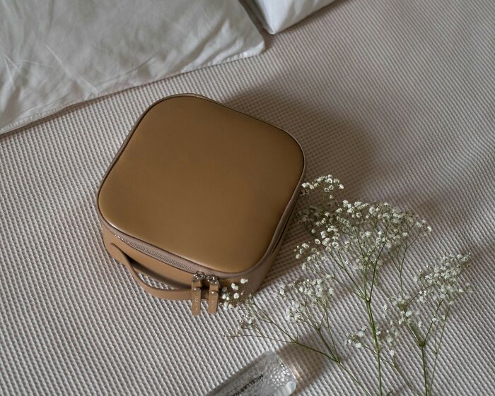 A beige travel bag on a bed with white flowers, showcasing game-changing essentials for easier traveling.
