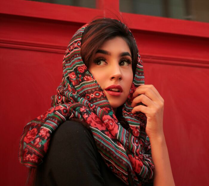 Person in a patterned headscarf against a red background, embodying peace and ease, related to traveling essentials.