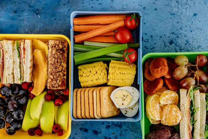 Colorful lunch boxes with fruits, sandwiches, and vegetables, illustrating self-paying-products with healthy food choices.