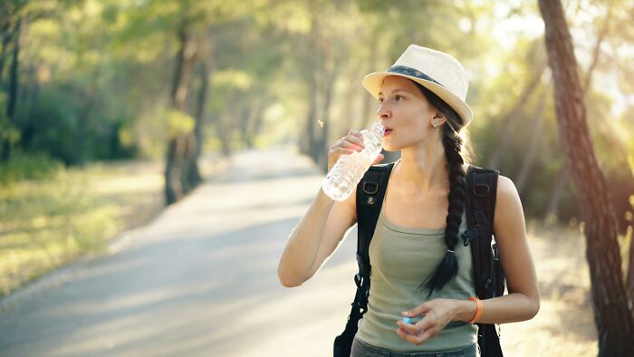 Woman hiking on a forest path, wearing a hat and backpack, highlighting shocking cultural differences in outdoor activities.