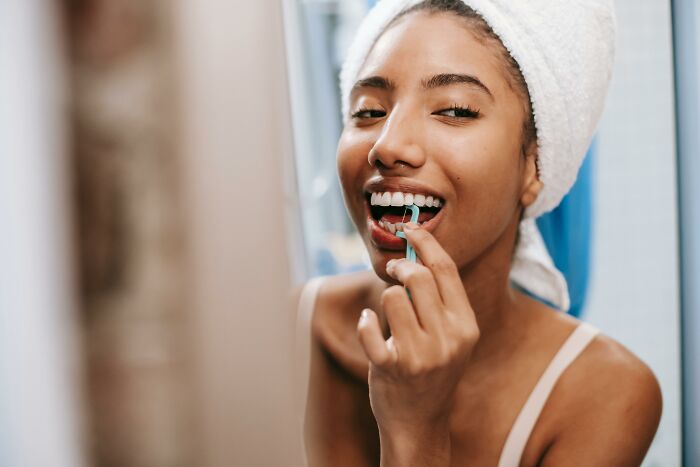 Person smiling and flossing teeth with a towel on their head, showcasing self-paying-products.
