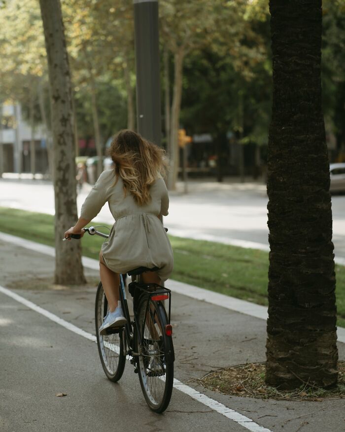 Person riding a bicycle on a tree-lined street, illustrating frugal lifestyle choices.