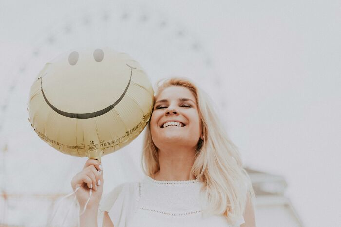 Woman smiling with a smiley face balloon, showcasing the world's weirder side. Woman smiling with a smiley face balloon, showcasing the world's weirder side.