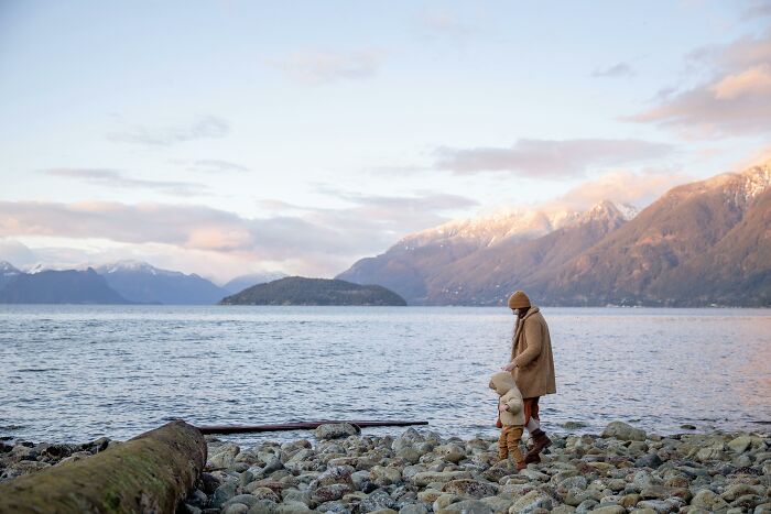 A person and child in warm clothing walk by a serene lake with mountains; 2025-Trends nature exploration.