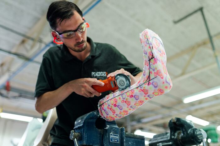 Man using power tool to shape a prosthetic leg with colorful heart patterns, highlighting real men doing skilled work.
