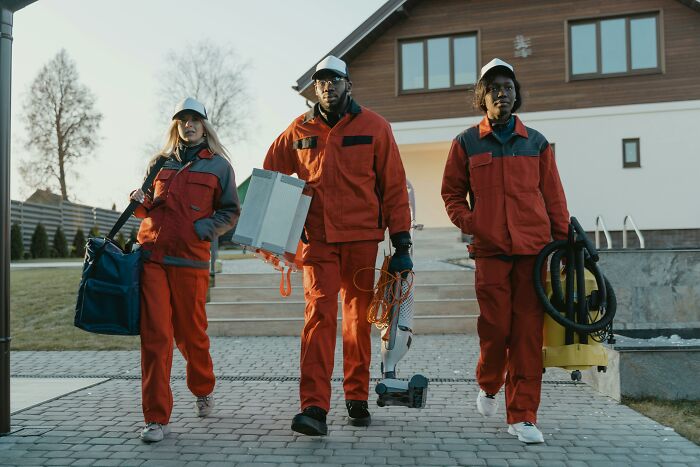 Three workers in red uniforms carrying tools and equipment, representing things associated only with rich people.