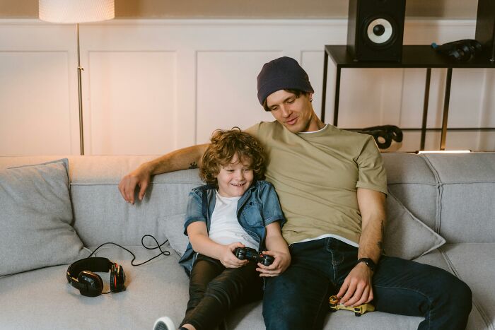 Father and son playing video games on a couch, sharing a memorable moment.
