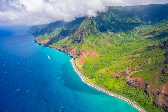 Aerial view of a lush, mountainous coastline meeting blue ocean, possibly linked to weird government projects.