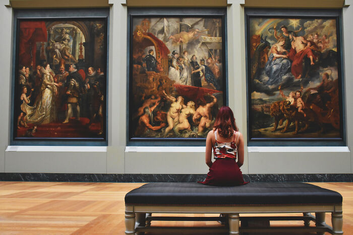 Woman sitting on a bench, viewing large paintings in a museum gallery; unique gift ideas for art lovers.
