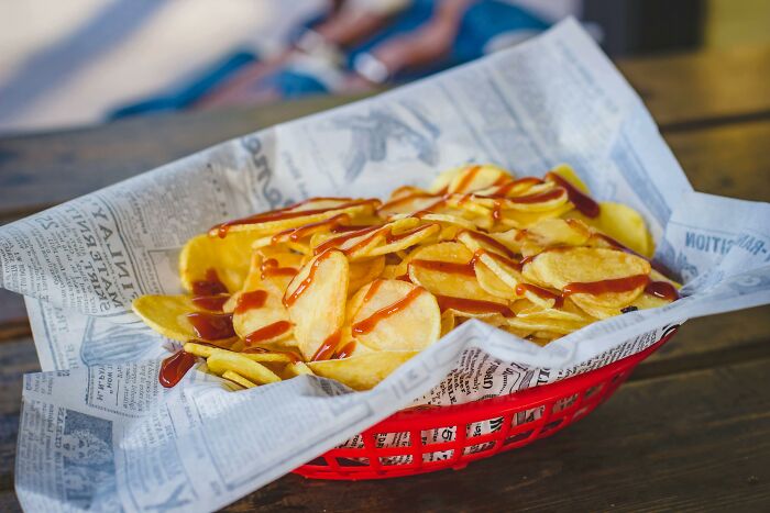 Basket of potato chips drizzled with sauce, served on newspaper in a red basket, highlighting deeply weird taste preference.