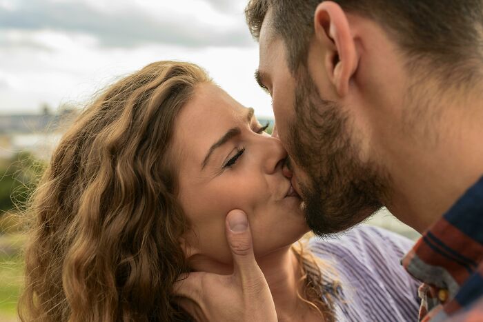 A couple shares an intimate kiss outdoors, capturing eye-opening moments of affection.