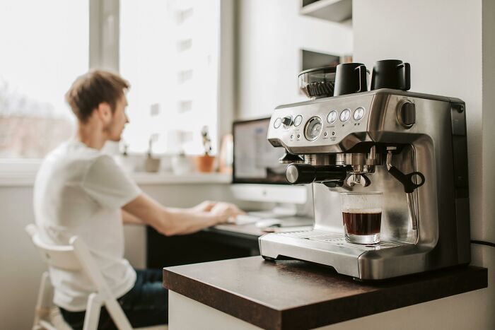 Coffee machine brewing espresso with person working in background, illustrating self-paying-products concept.