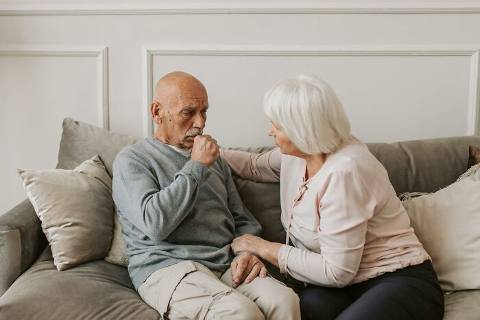 Elderly couple sitting on a sofa, engaged in a conversation.