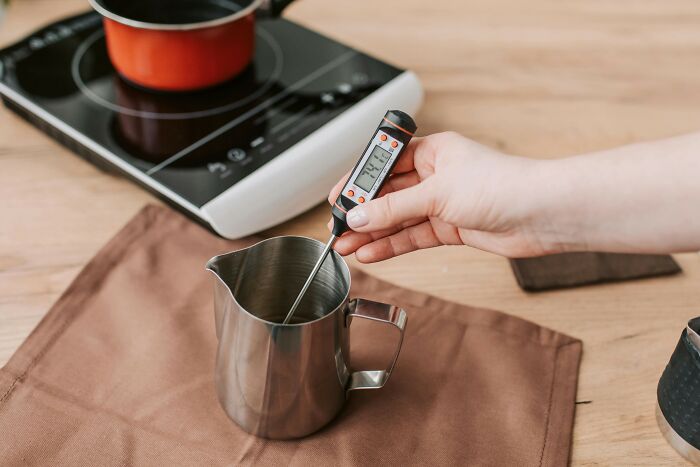 Person using a digital thermometer in a metal jug, with an induction stove in the background, showcasing a practical gift idea.