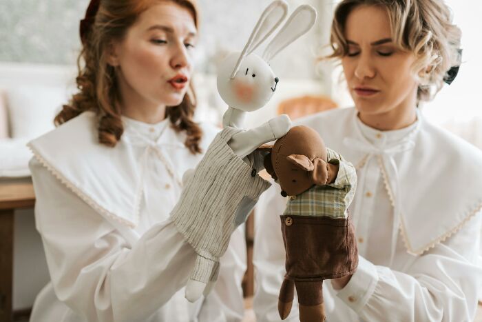 Two women using hand puppets, depicting work-struggles in a creative setting.