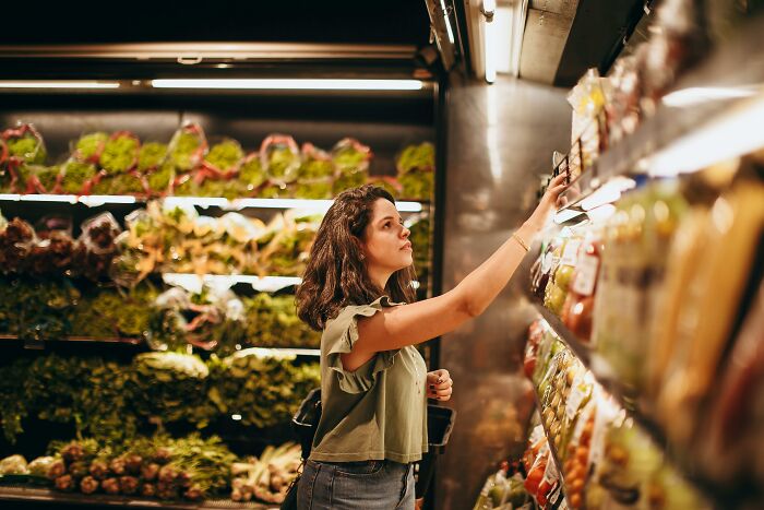 Woman shopping in a grocery aisle, examining self-paying-products in a well-lit store environment.