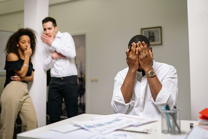 Man experiencing work struggles at desk, two colleagues looking on concerned.